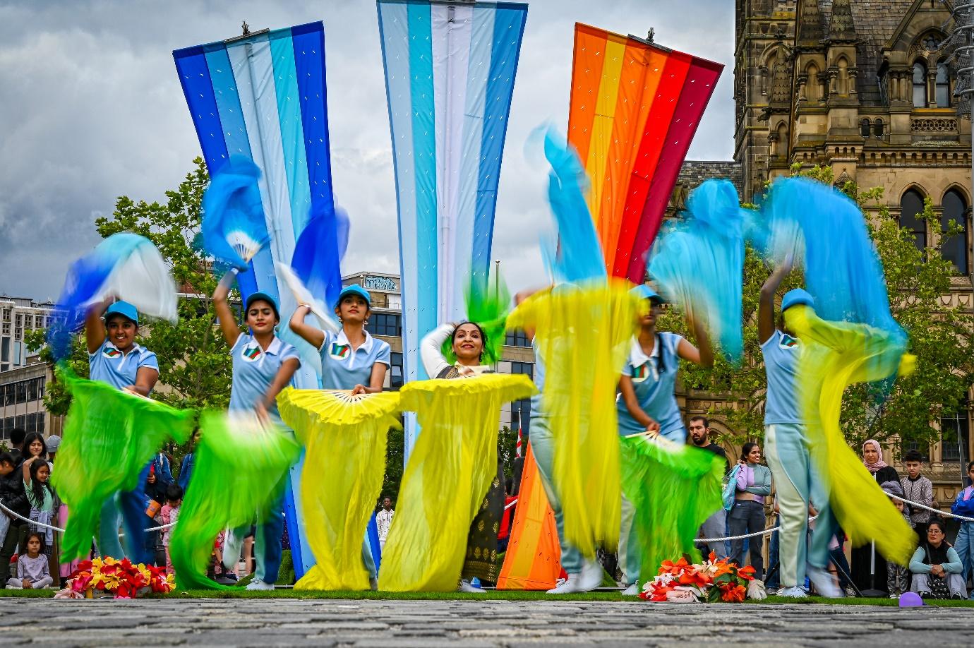 A group of people dancing with colorful flags

Description automatically generated